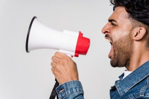 man-in-blue-denim-jacket-holding-a-megaphone-5935755 Close-up side view of a man shouting passionately into a megaphone, expressing urgency.